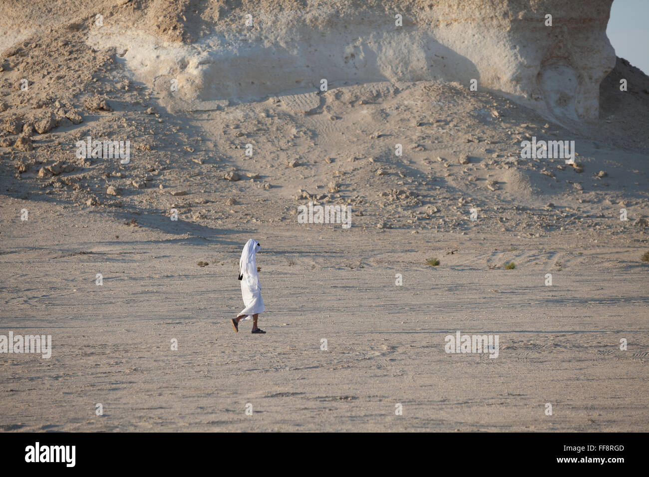 Lone Arab man walking in Qatar desert in traditional white robe, thawb