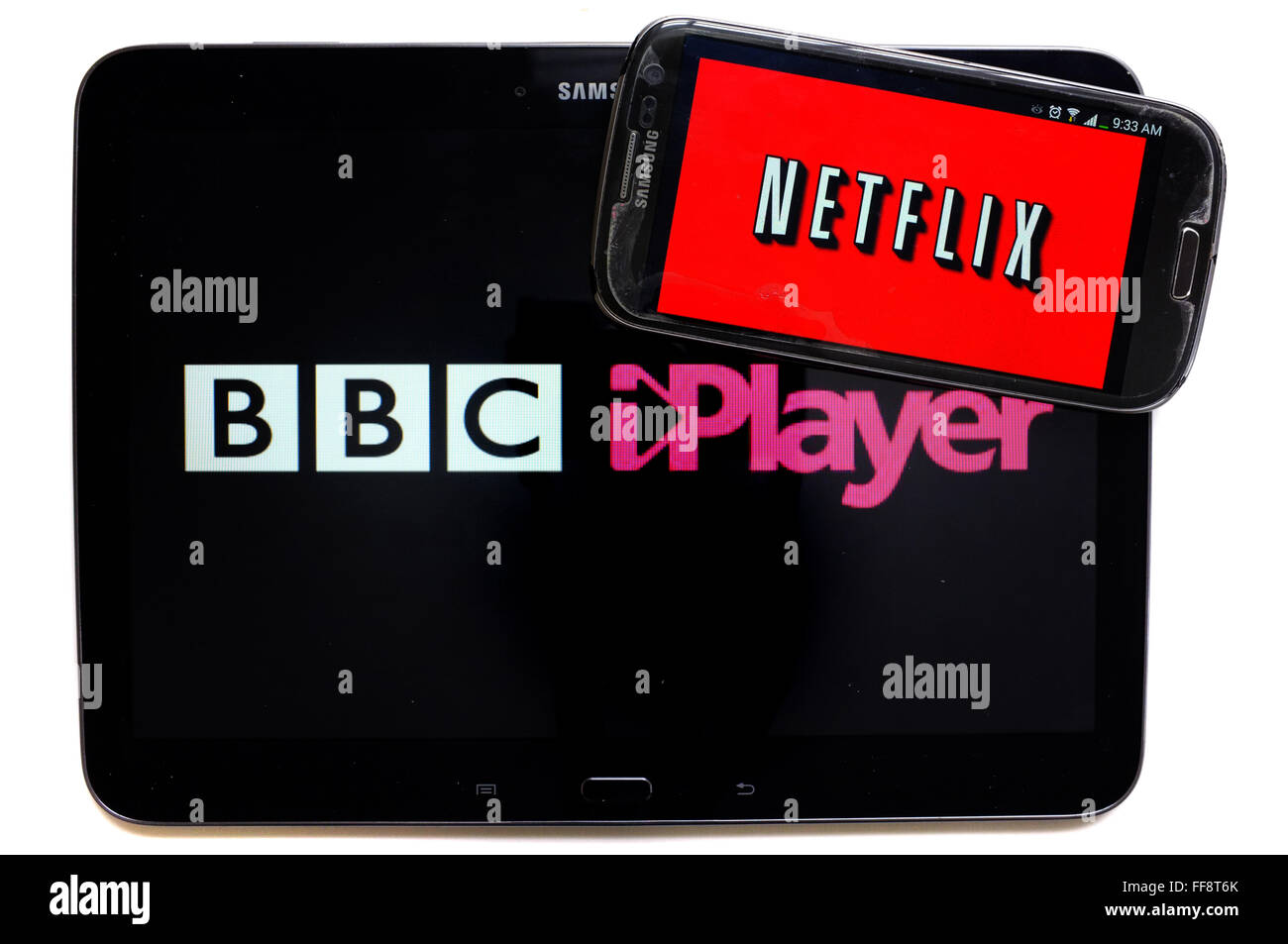 The Netflix logo on a smartphone screen on top of a tablet displaying the iPlayer logo photographed against a white background. Stock Photo