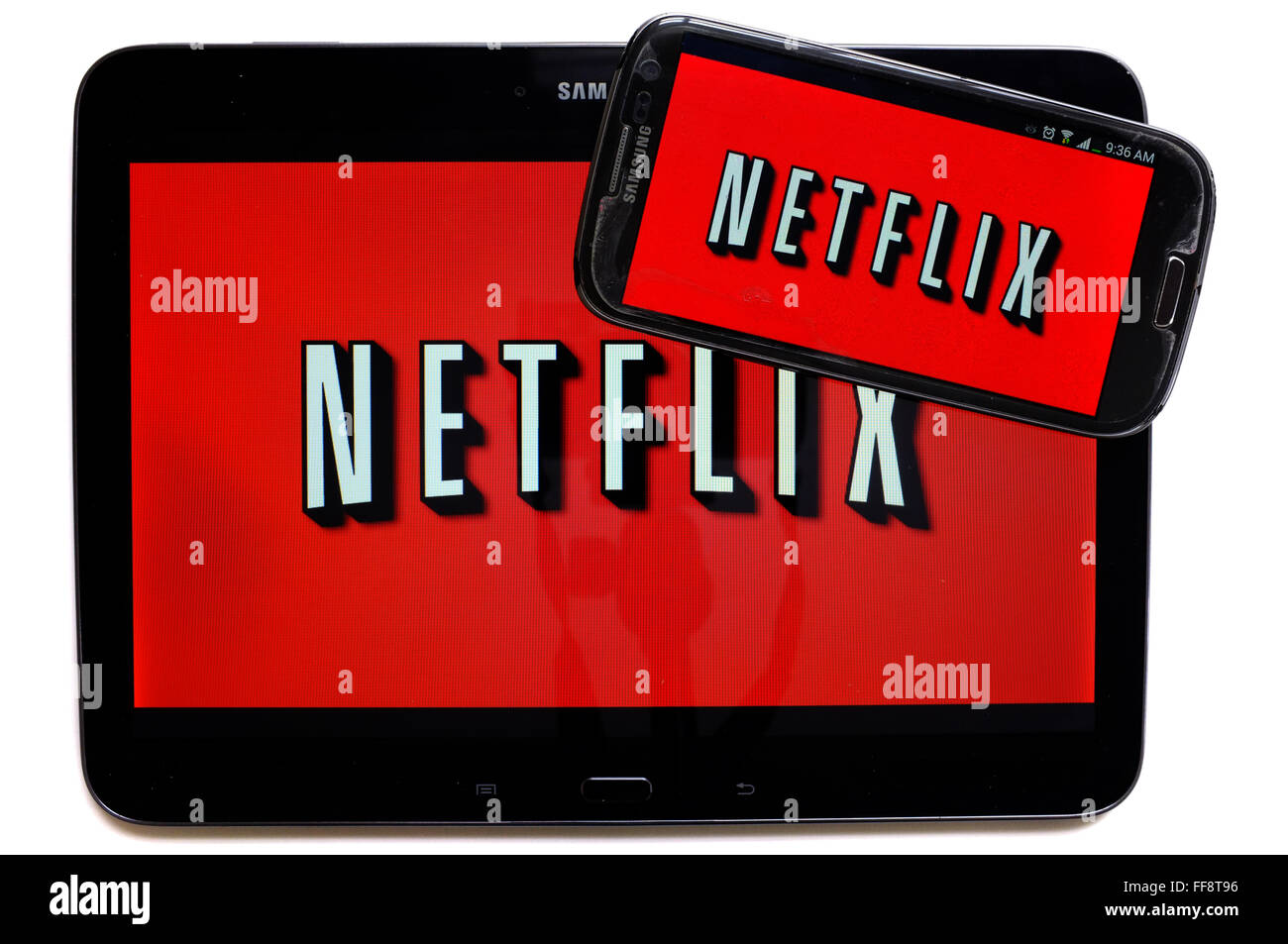 The Netflix logo on a smartphone screen and a tablet photographed against a white background. Stock Photo