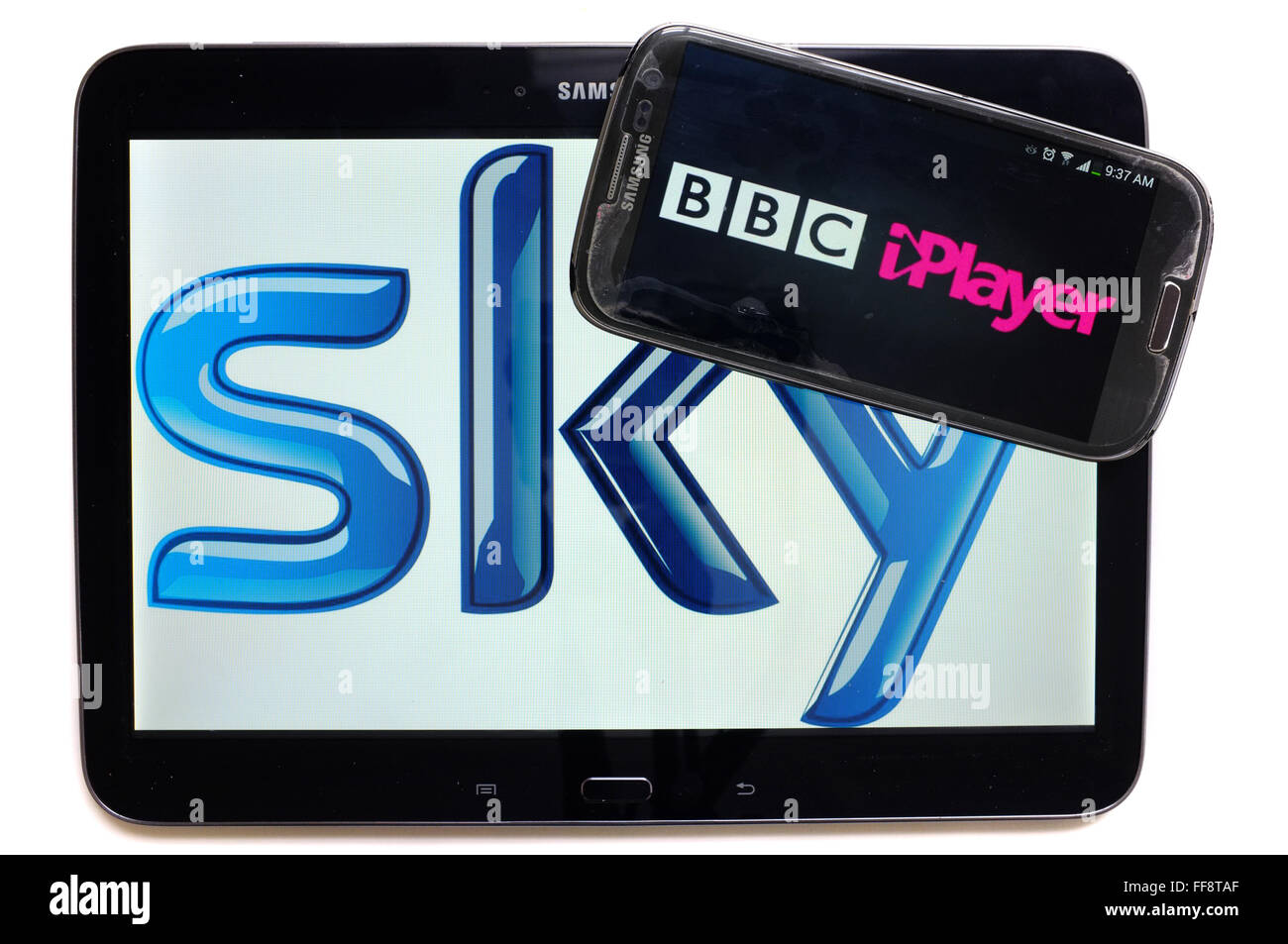 The BBC iPlayer logo on a smartphone screen on top of a tablet displaying the Sky logo photographed against a white background. Stock Photo