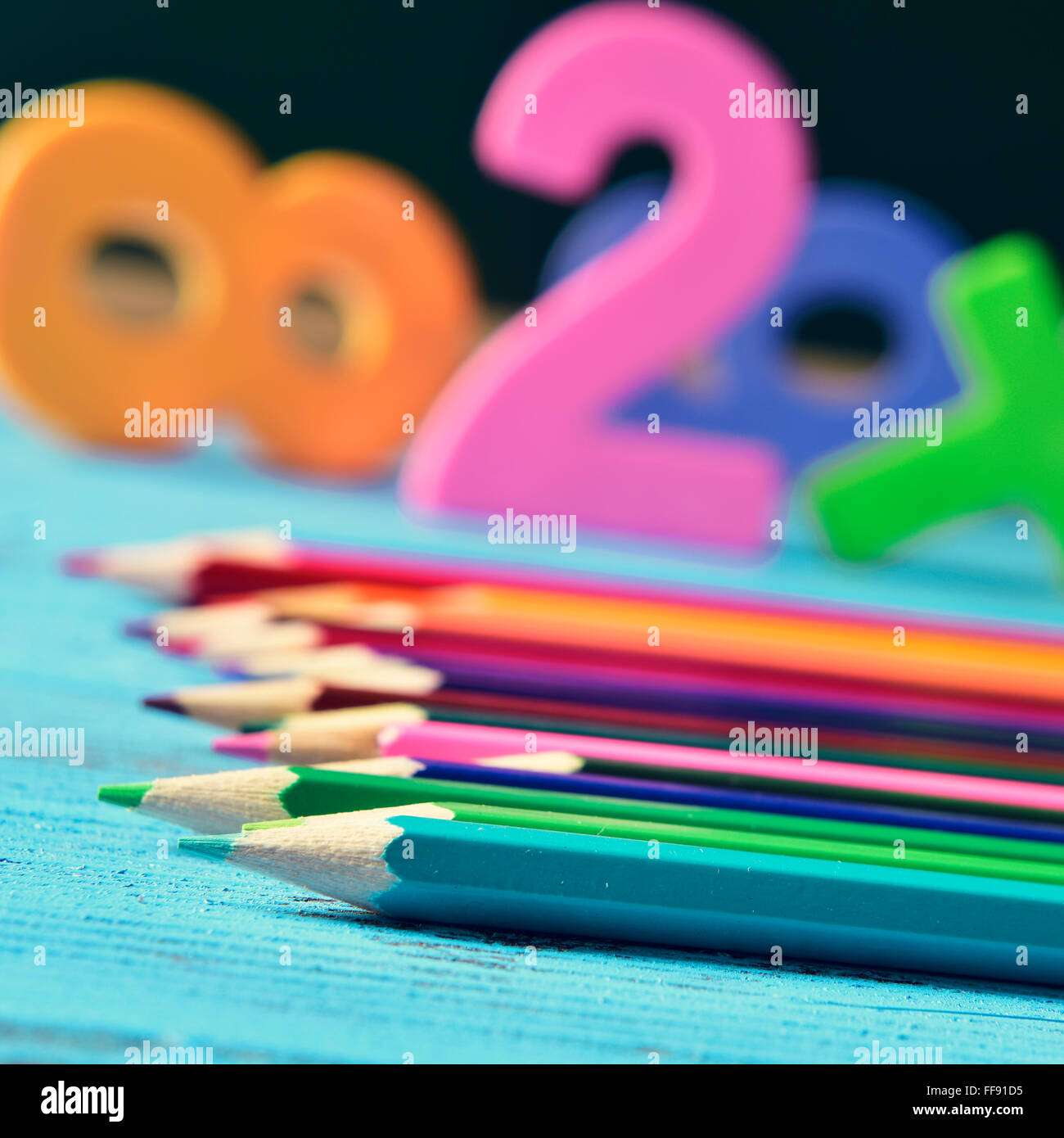 closeup of a pile of pencil crayons of different colors and some numbers on a blue rustic wooden table in a classroom Stock Photo