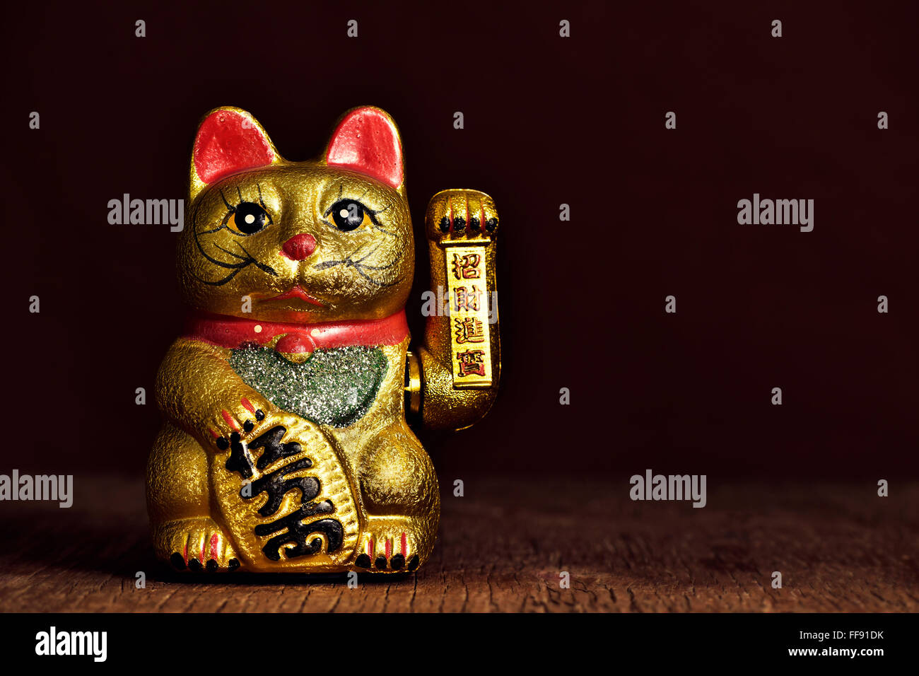 a golden chinese lucky cat with its left paw raised, on a rustic wooden surface Stock Photo