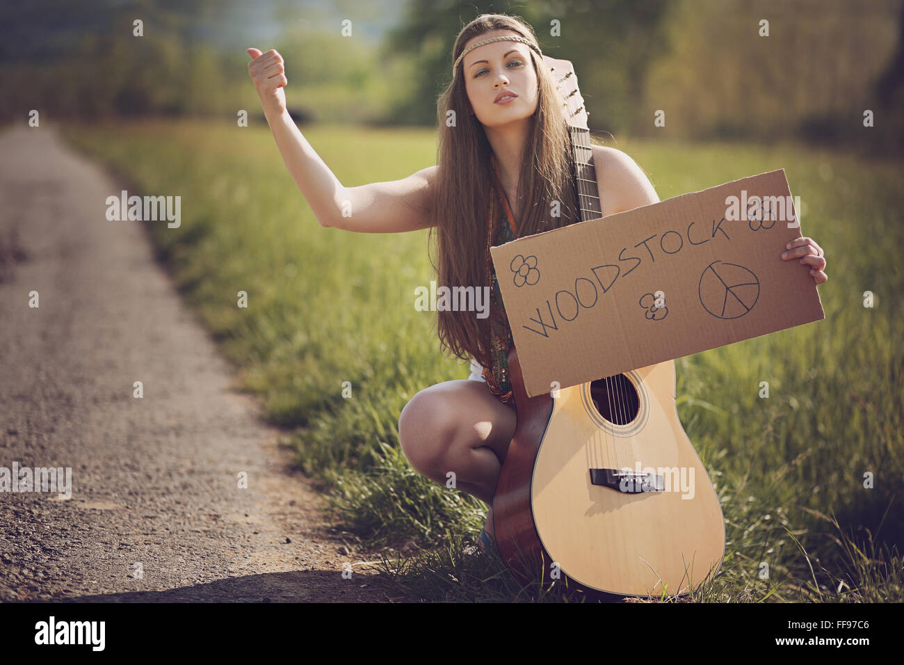 Beautiful hippie with guitar hitch-hiking for Woodstock . Warm summer tones Stock Photo
