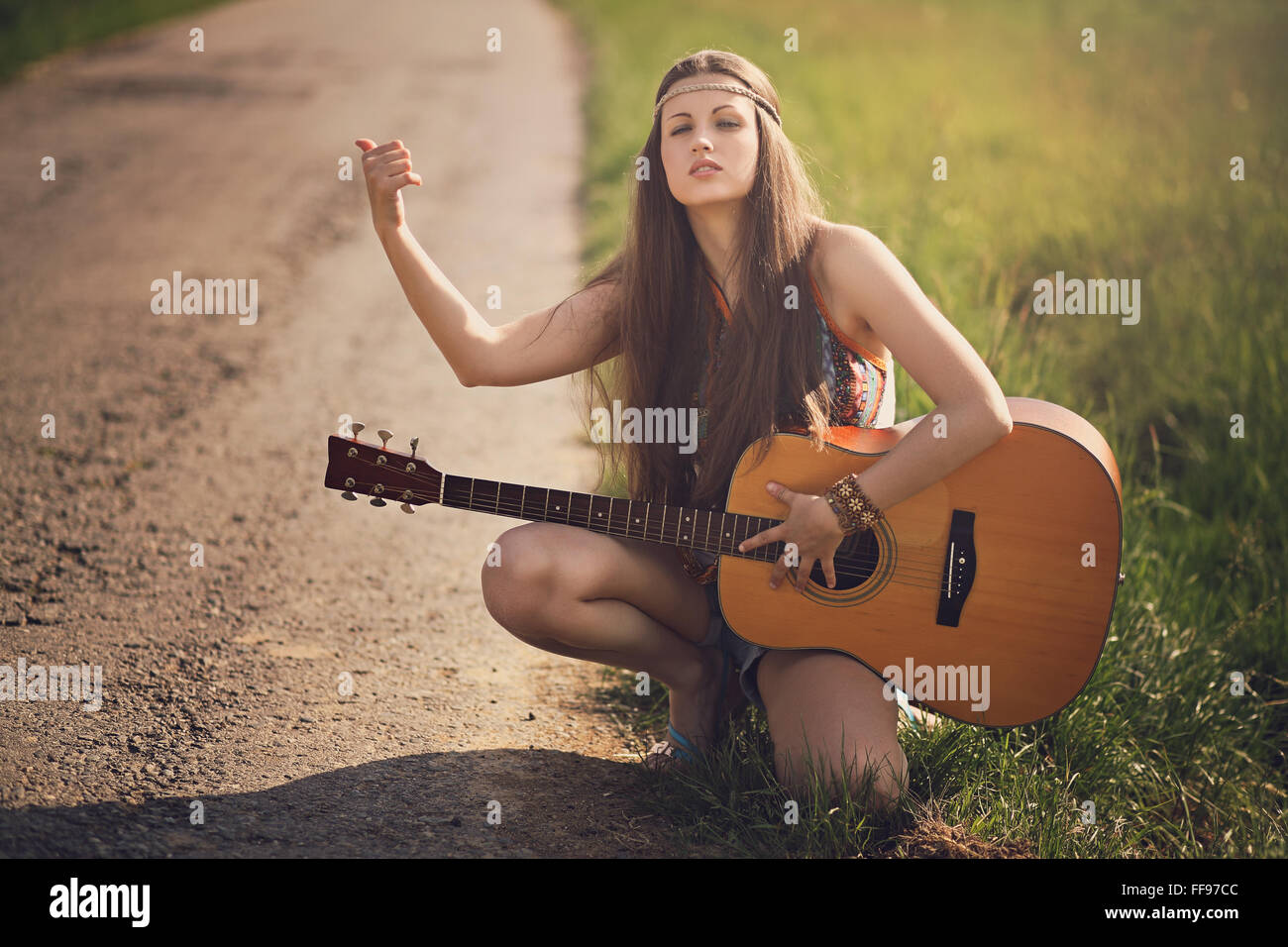 Beautiful hippie hitch-hiker with guitar . Warm summer tones Stock Photo