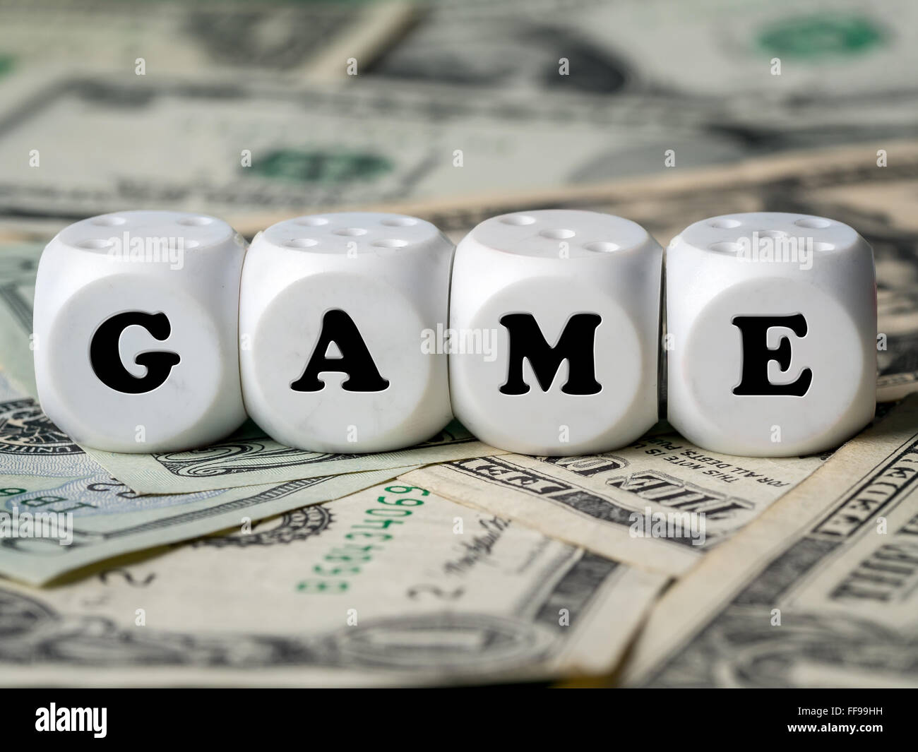 Four white dice placed on pile of money spelling GAME word Stock Photo