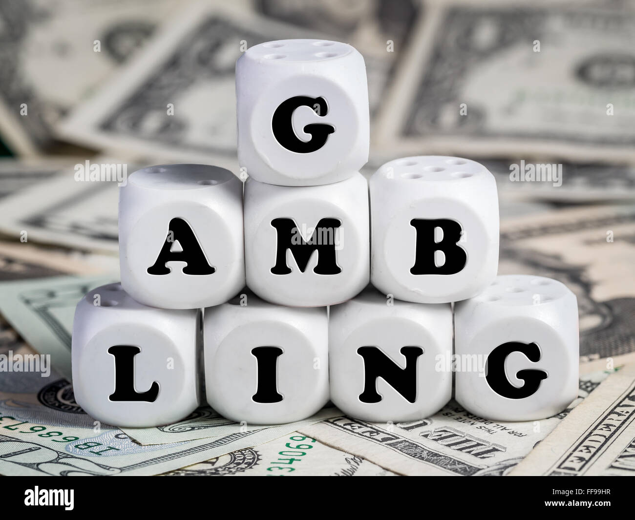 Eight white dice placed on pile of money spelling GAMBLING word Stock Photo