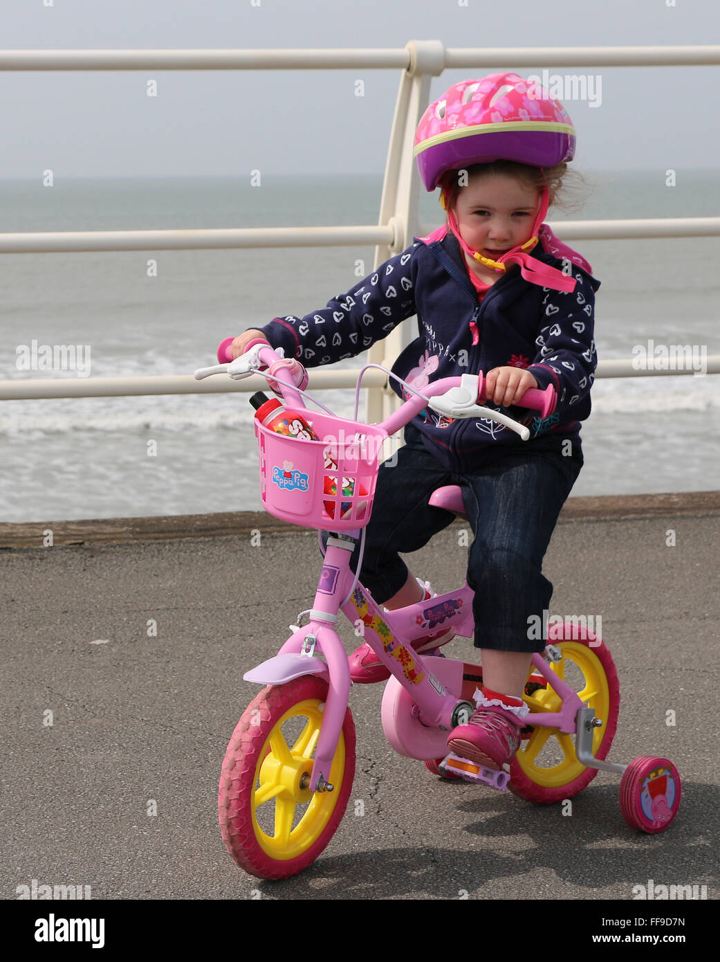 Young girl learning to ride bicycle, wearing a safety helmet, Aberavon Beach, Wales, UK Stock