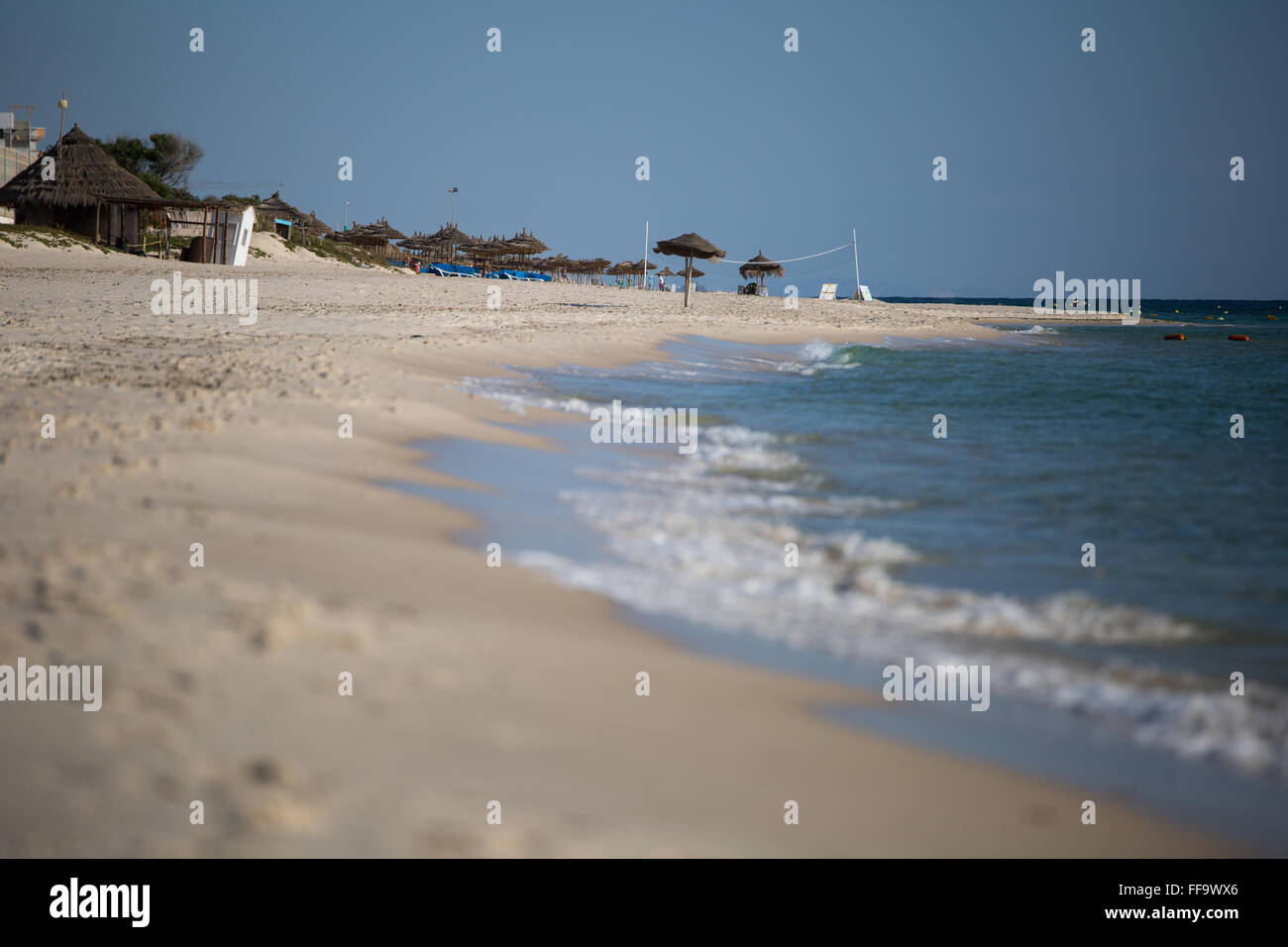 Morning view of a beach in Tunisia, water's edge in the foreground, beach umbrellas and chairs far in the distance Stock Photo