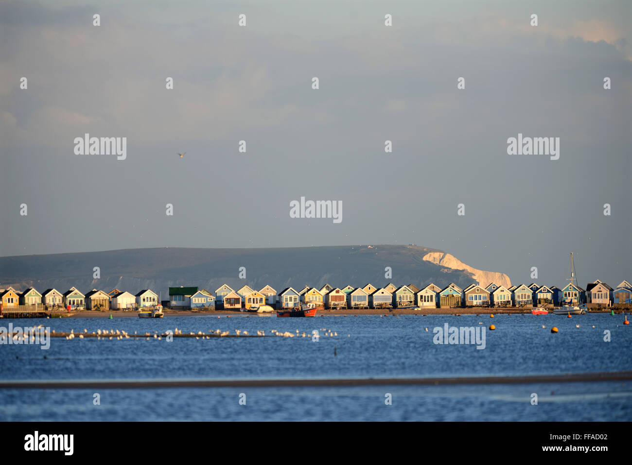 Beach huts at Mudeford quay or spit with Christchurch harbour in the foreground and the Isle of Wight in the background. Stock Photo