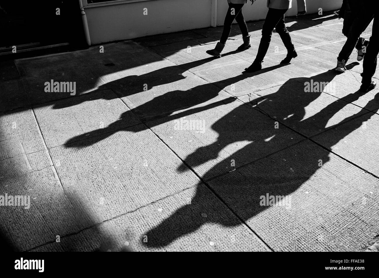 Shadow of four walking pedestrians projected on the sidewalk Stock Photo