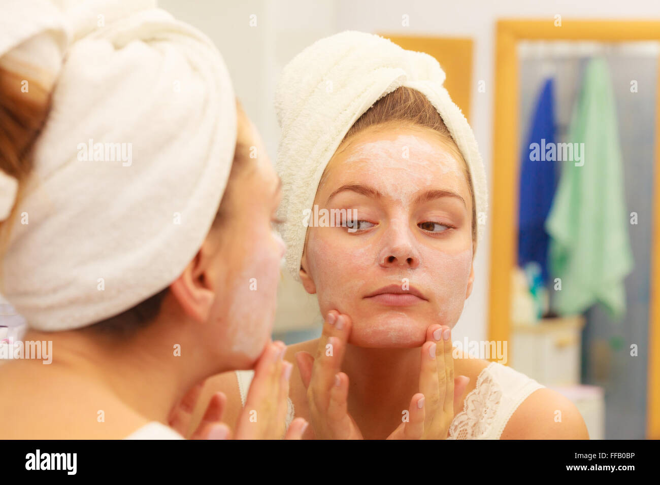 Woman applying mask moisturizing skin cream on face looking in bathroom