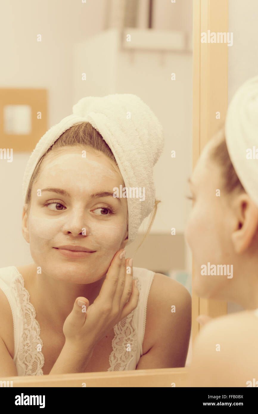 Woman applying mask moisturizing skin cream on face looking in bathroom