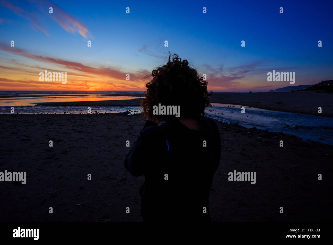 Sunset photos being shot by a woman with a camera on the beach at dusk. Stock Photo