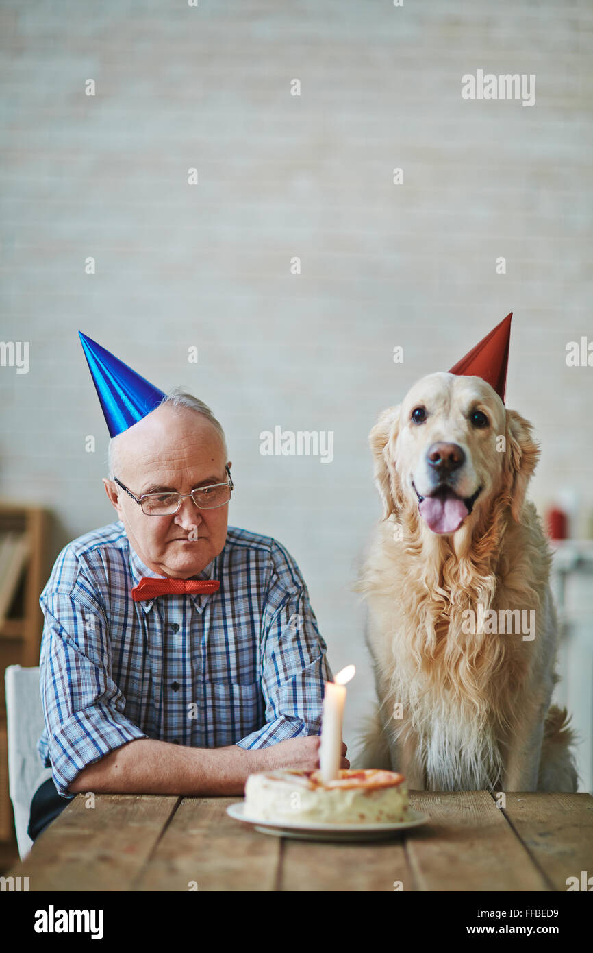Mature man and his pet sitting by table with birthday cake with burning