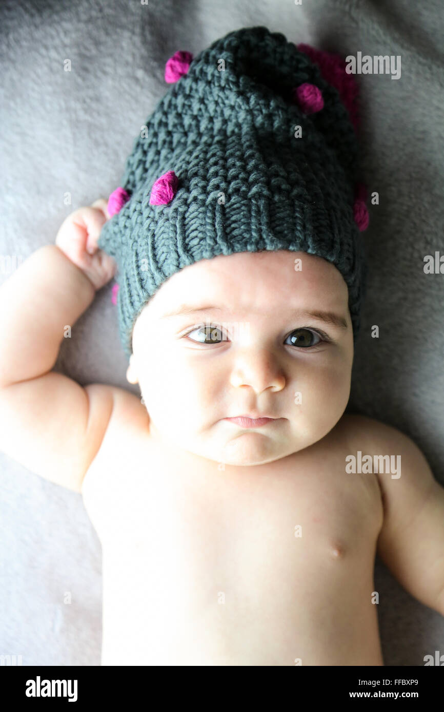 cute baby's portrait with chubby cheek's lying in bed while wearing a wool cap, Stock Photo