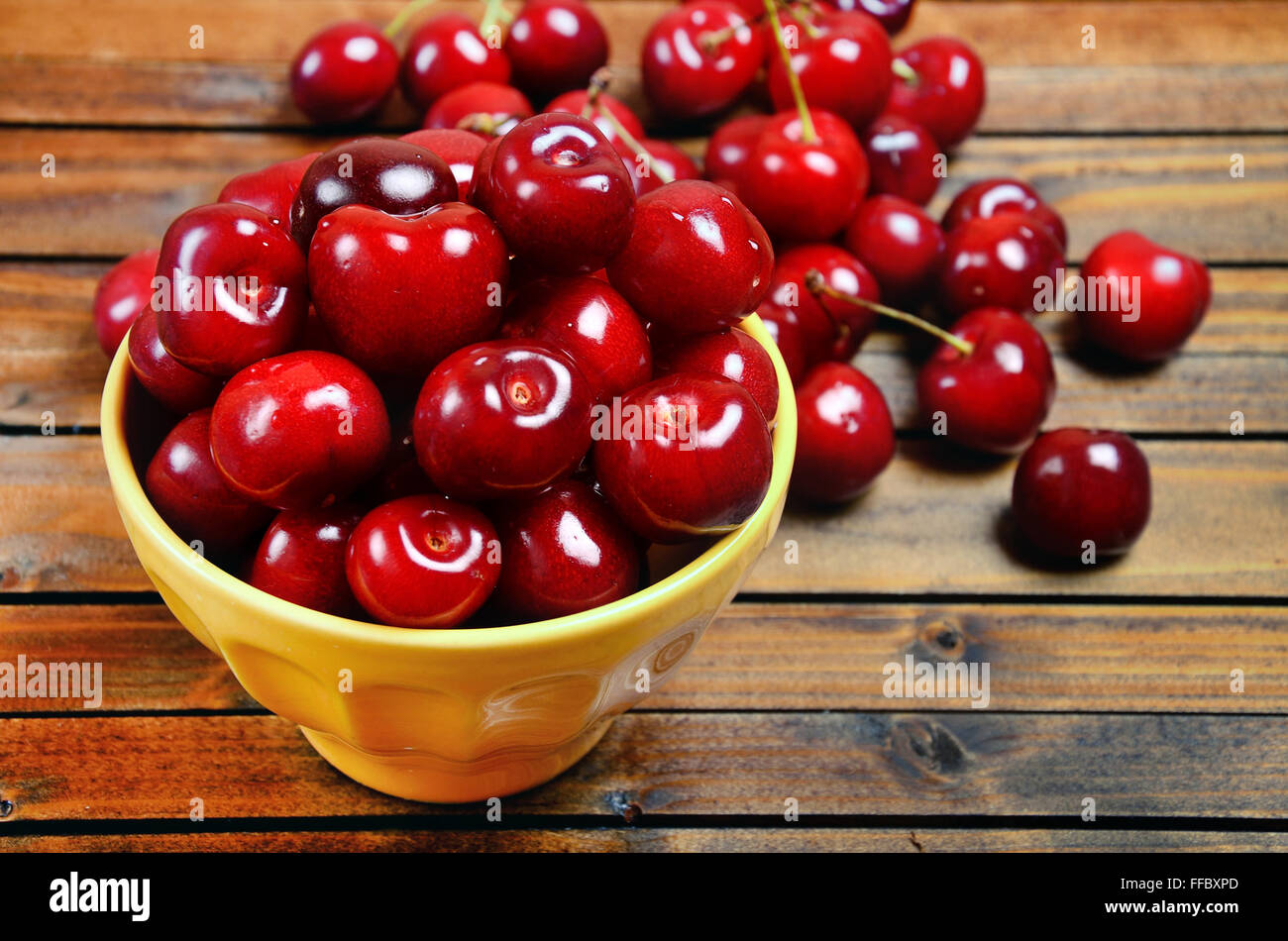 Yellow bowl with cherries on wooden table Stock Photo