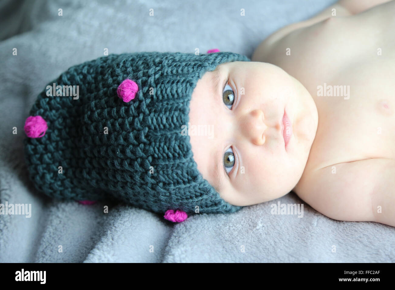 cute baby's portrait with chubby cheek's lying in bed while wearing a wool cap Stock Photo