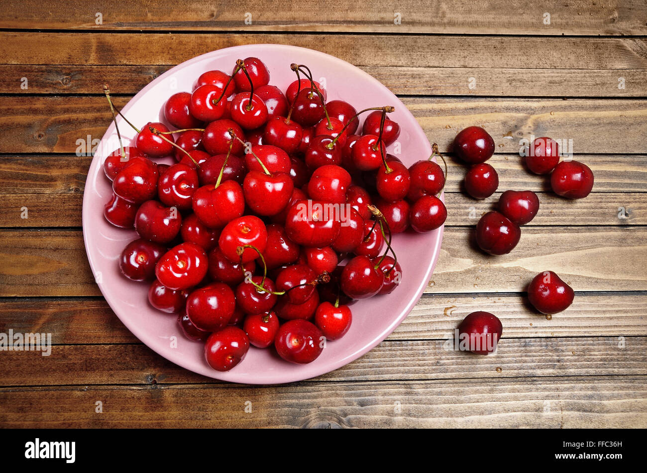 Pink plate with cherries on wooden table Stock Photo