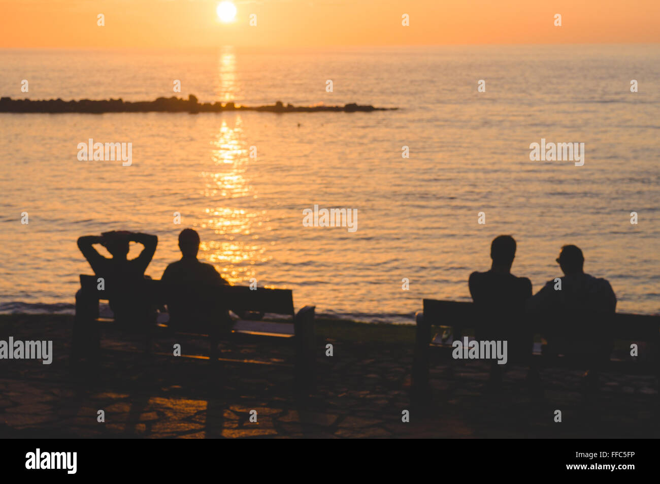 Silhouette of people sitting on bench and enjoying sunset, blurred image with matt toning Stock Photo