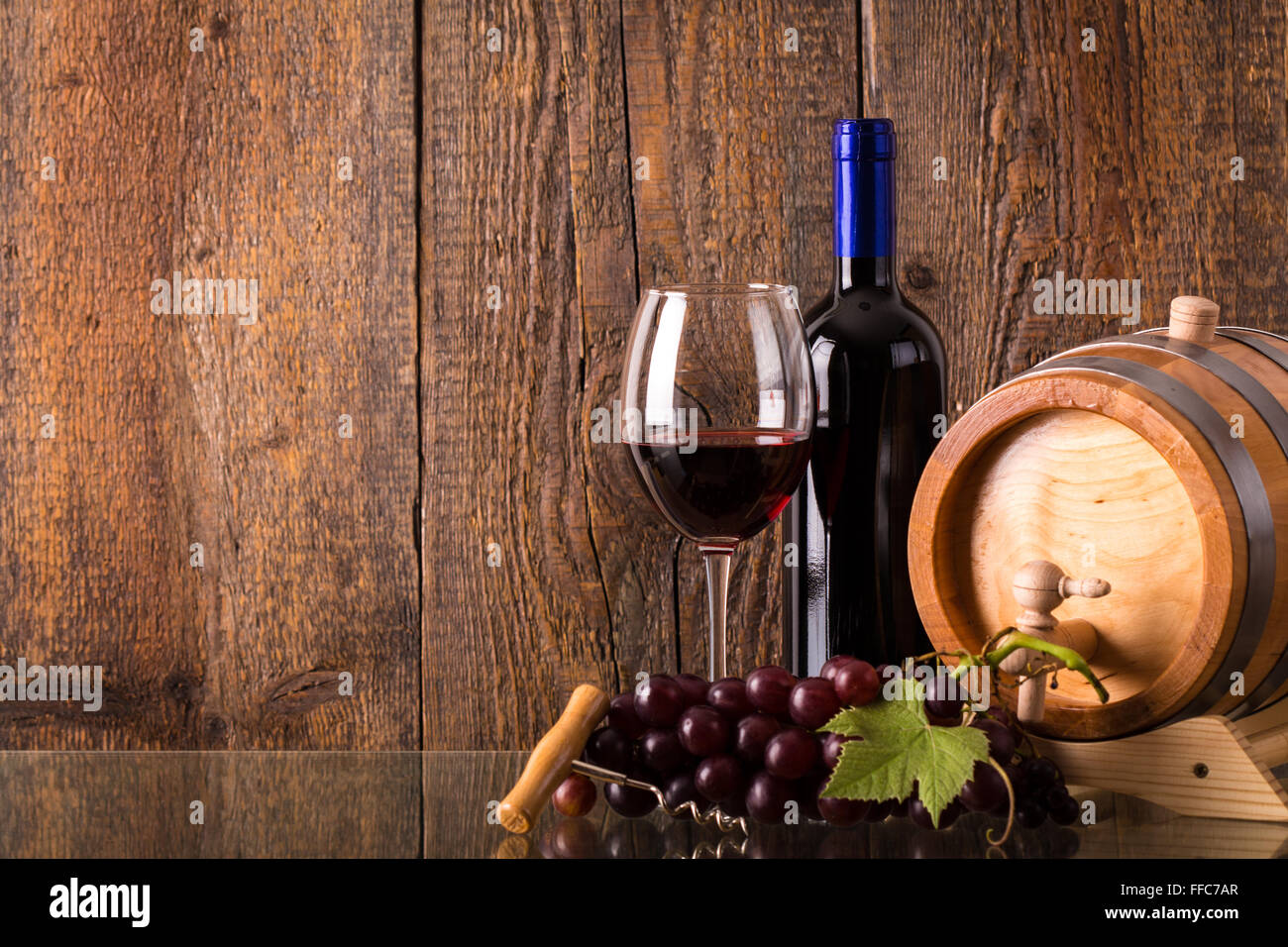 Glass of red wine with bottle barrel grapes and wooden background Stock ...