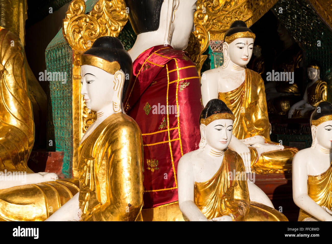 Close up of different sized golden Buddhas, one with a silky red cloak at the Shwedagon pagoda in Yangon Stock Photo