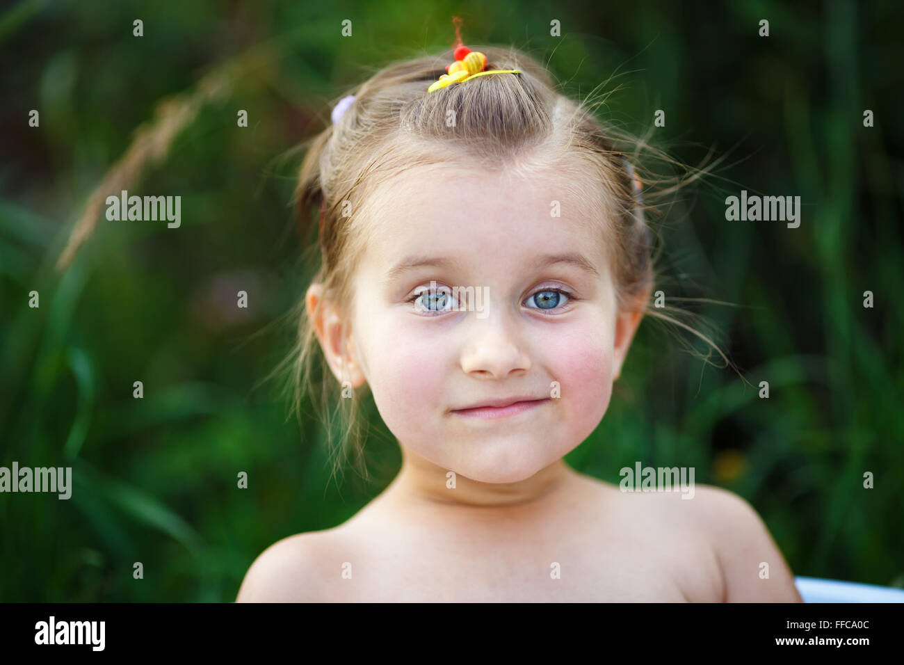 Close-up portrait of a little girl with blue eyes on the blurred green ...