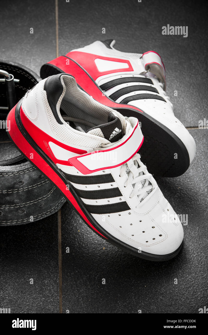 Adidas Olympic weightlifting shoes on a grey tiled floor with a weightlifting belt. Stock Photo