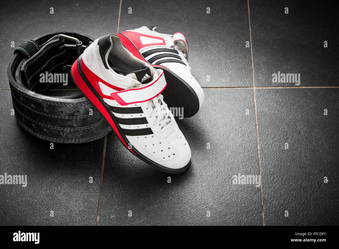 Adidas Olympic weightlifting shoes on a grey tiled floor with a weightlifting belt. Stock Photo