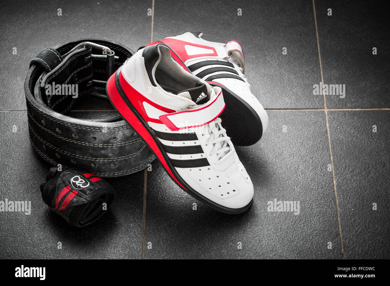 Adidas Olympic weightlifting shoes on a grey tiled floor with a  weightlifting belt and wrist straps Stock Photo - Alamy