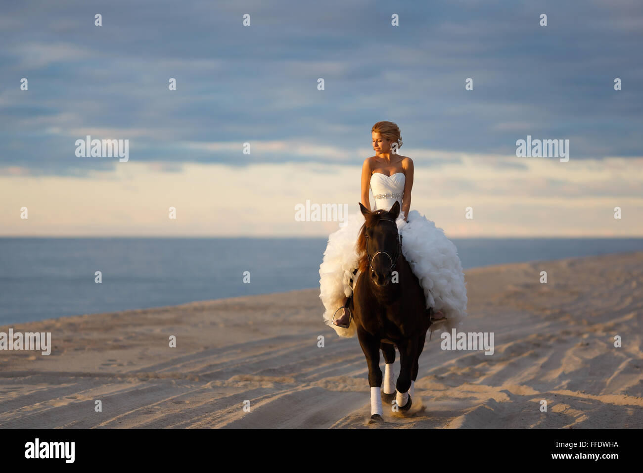 Bride on a horse at sunset by the sea in their wedding day Stock Photo