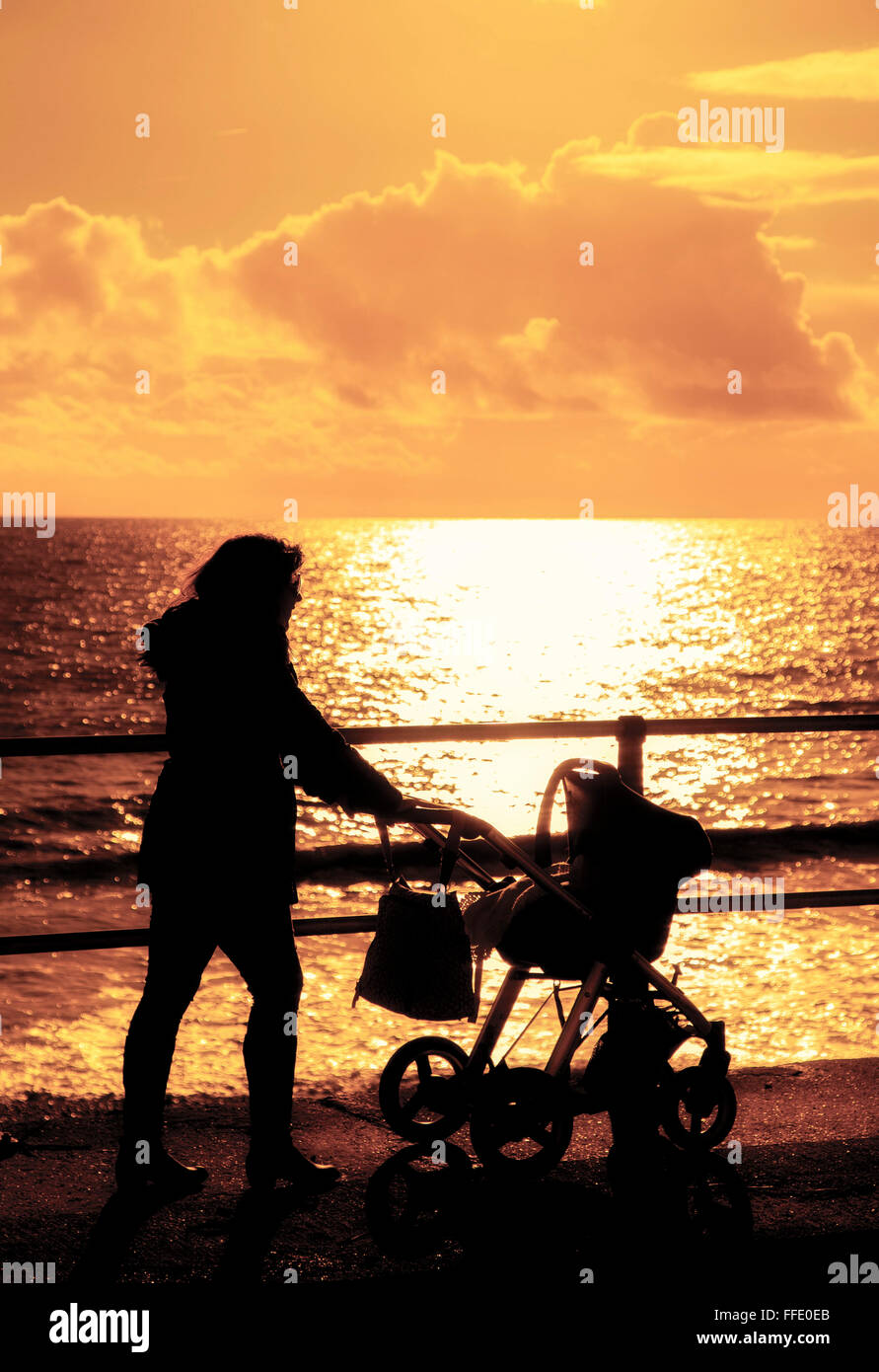 Mum with pram walking along sea front silhouette sunset Stock Photo
