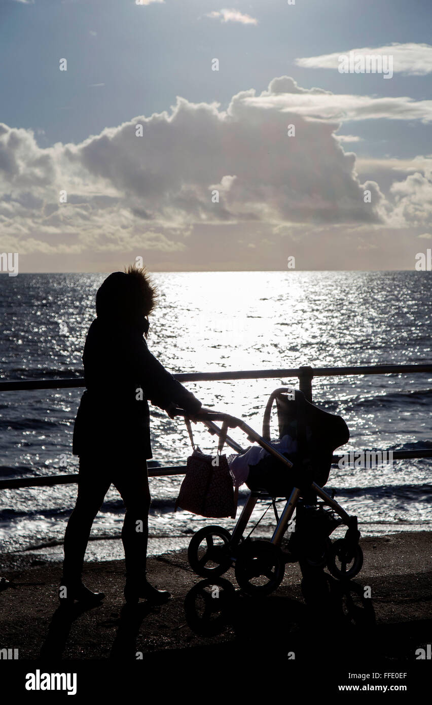 Mum with pram walking along sea front silhouette in winter Stock Photo