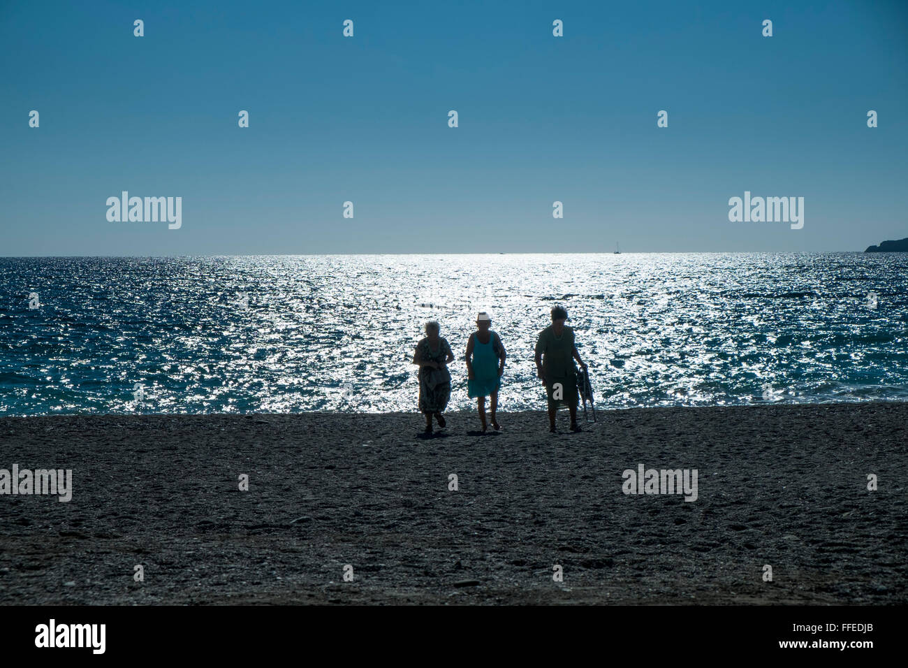 Three women walking on the beach late afternoon, backlit with a shimmering, sunlit sea. Almuñécar, Granada Province, Andalucia. Spain Stock Photo