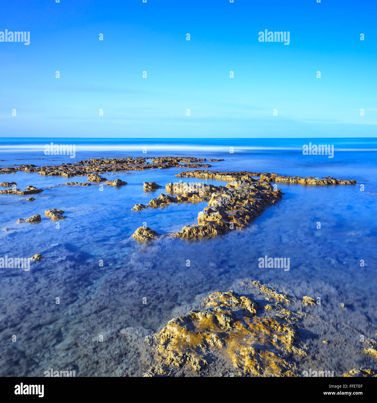 Rocks in a blue ocean under a clear sky on sunrise at morning. Tuscany, Italy. Long exposure photography Stock Photo