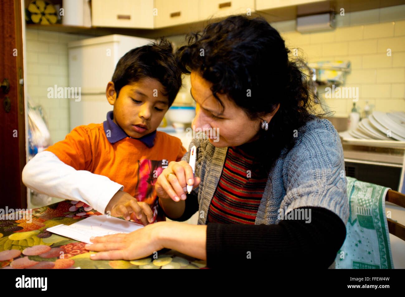Mature caucasian woman helps her adopted latin boy with his homework Stock Photo