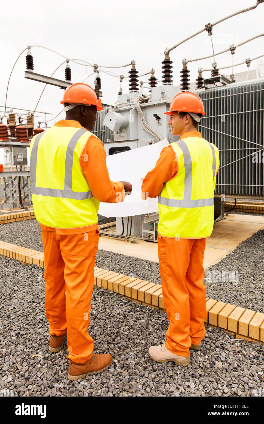rear view of industrial engineers discussing blueprint at substation Stock Photo