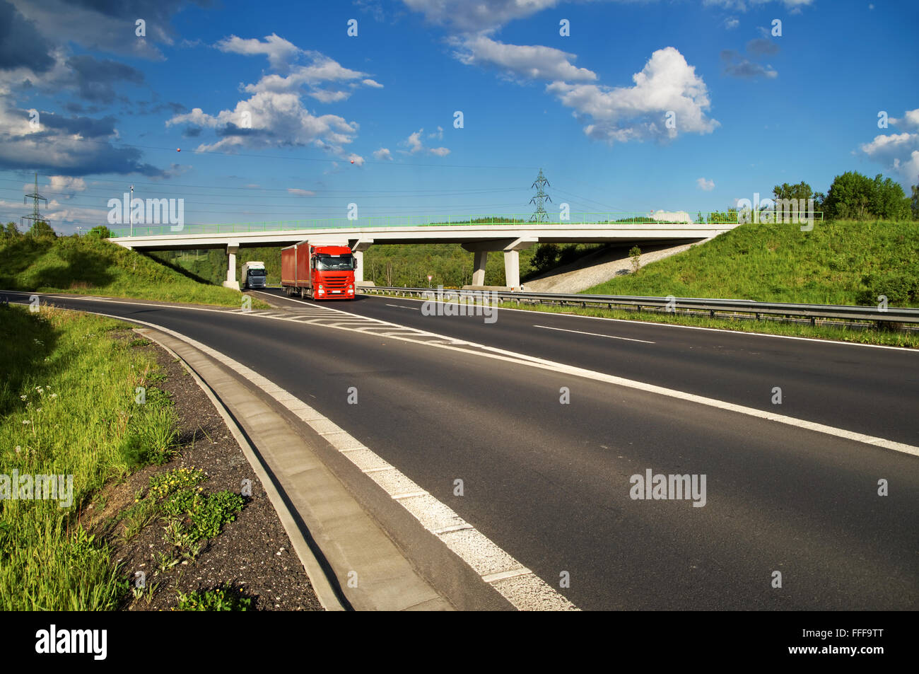 Bridge over an empty highway in the countryside, under a bridge passing two trucks, blue sky with white clouds Stock Photo