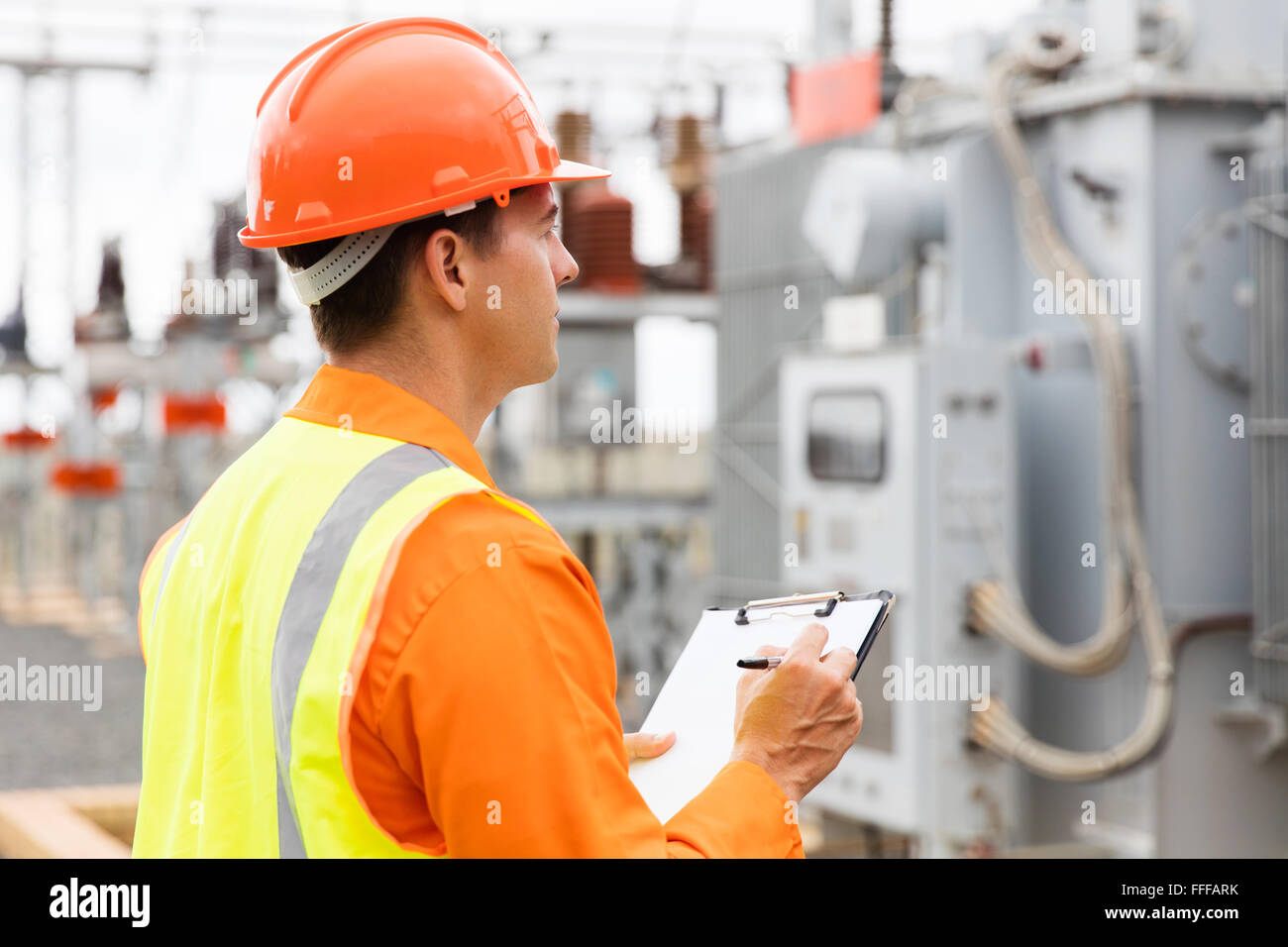side view of electrical engineer writing on clipboard in substation Stock Photo