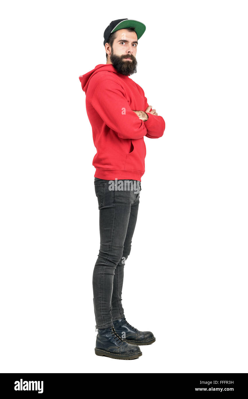 Side view of young bearded man in red hoodie wearing baseball cap with