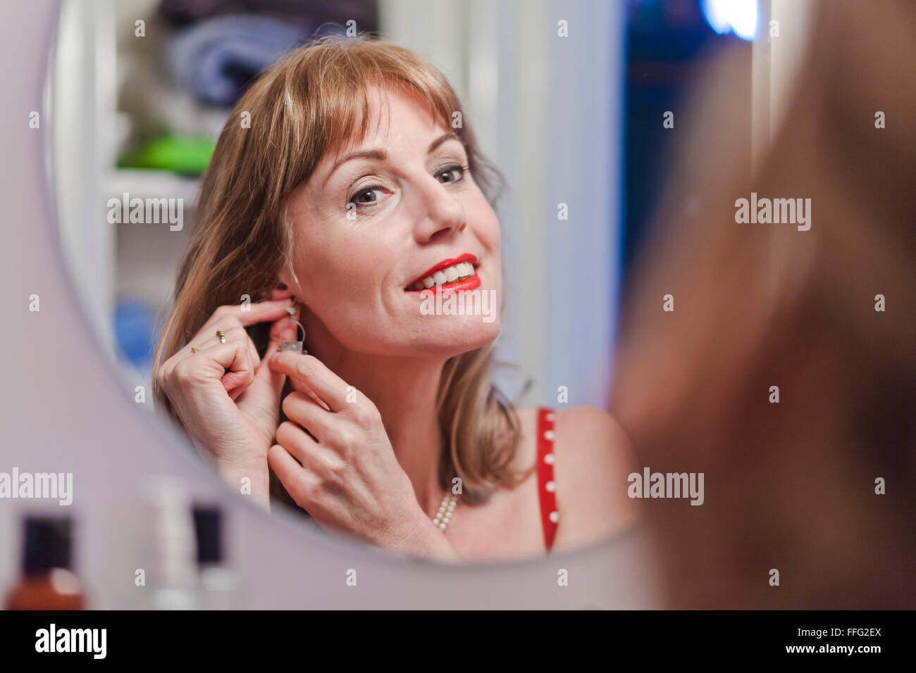 Mature woman putting on earring. Stock Photo