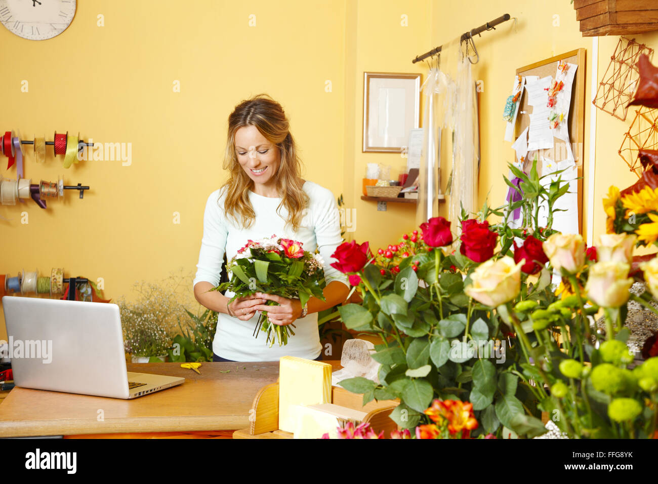 Small business owner. Portrait of mature florist standing in her small flower shop behind the laptop while preparing flowers Stock Photo