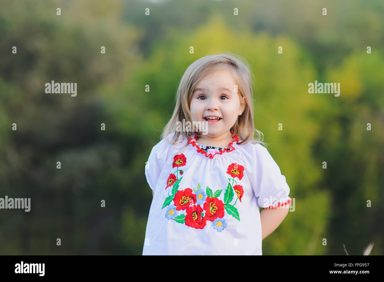 Little 3-year-old girl  emotionally rejoices. A girl dressed in white Ukrainian national dress with embroidered flowers. Stock Photo