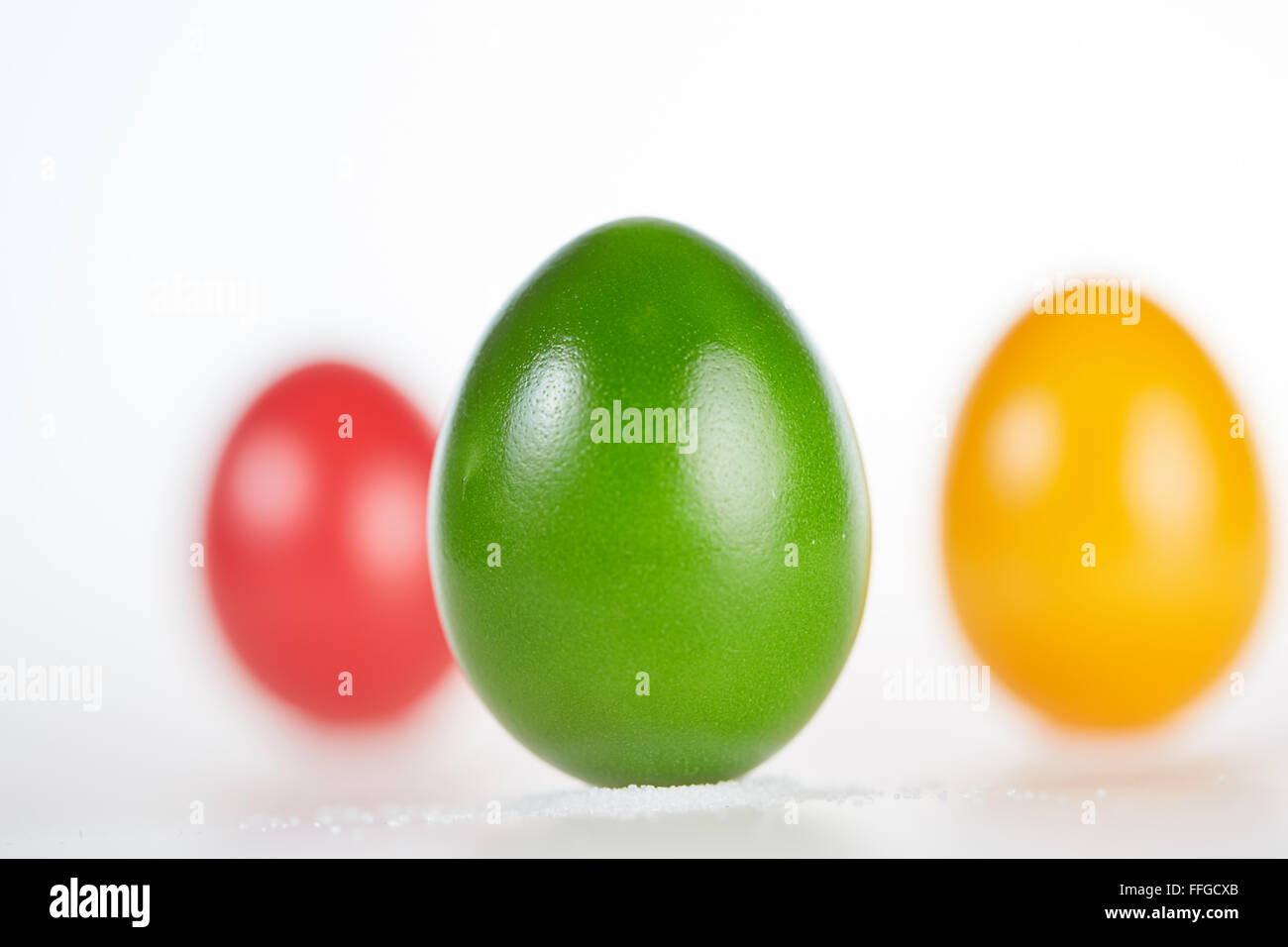 Three colored easter eggs standing on a white background on little pile of salt Stock Photo