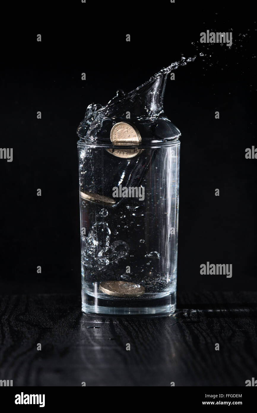 British Pound coins dropped into a glass of water. Stock Photo