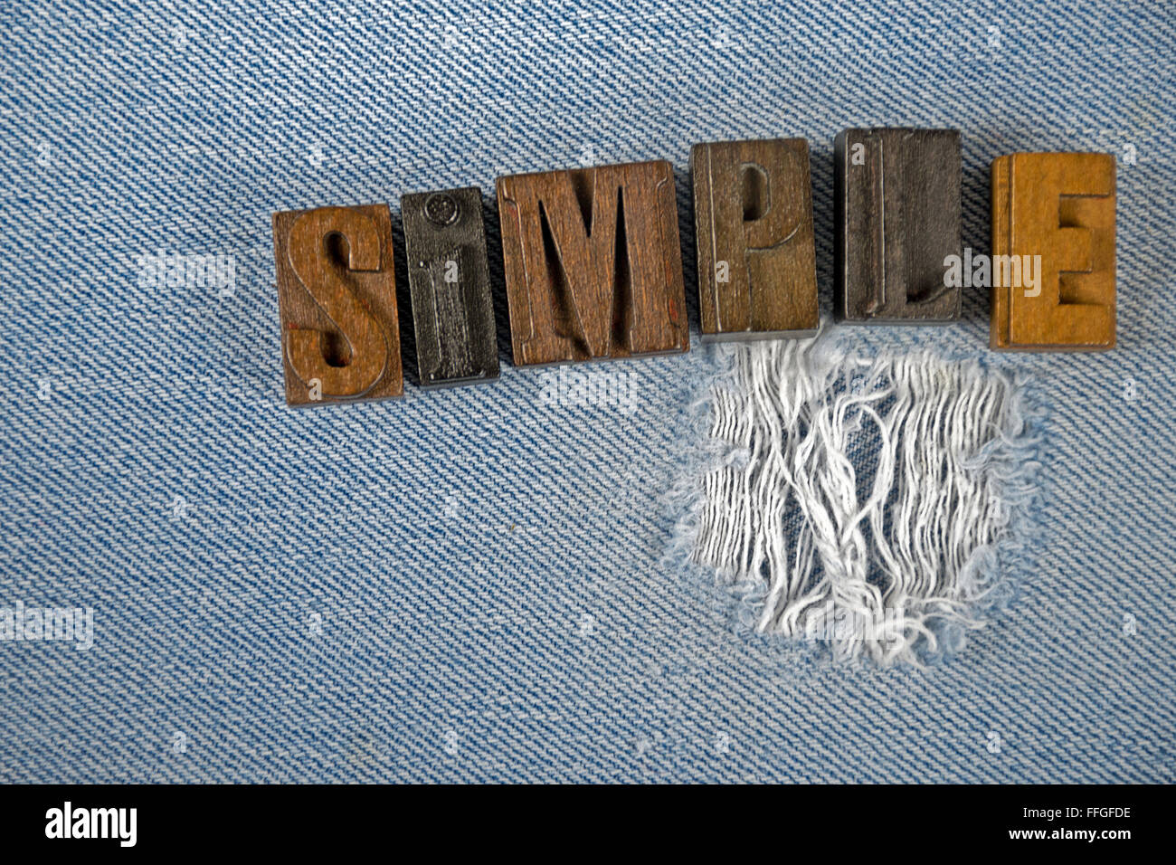The word simple in wooden letterpress type on frayed denim fabric. Stock Photo