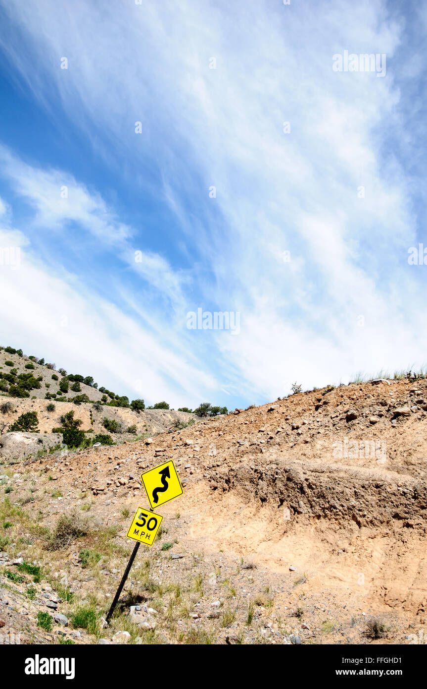 Speed limit sign on a curvy, rocky road with blue sky and clouds Stock Photo