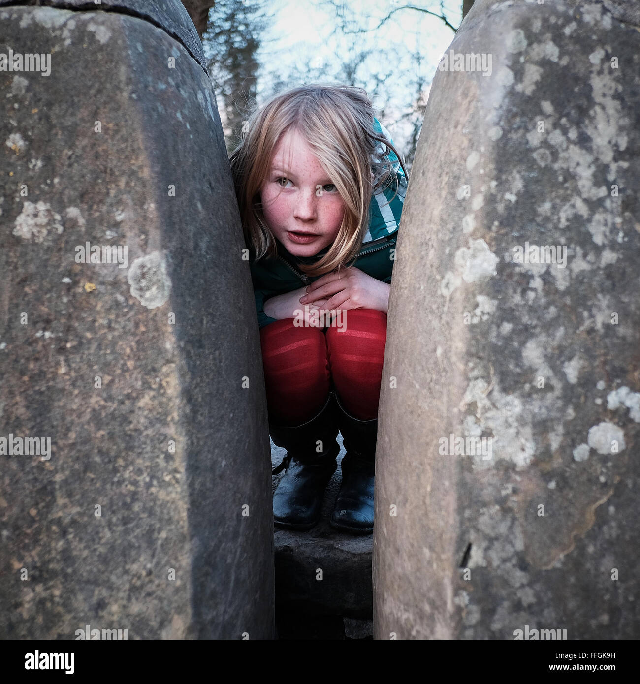 Girl crouching down between two stones Stock Photo - Alamy
