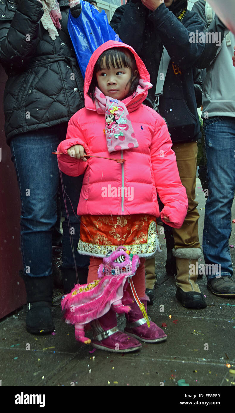 A beautiful 5 year old Chinese girl in a fancy dress & a small dragon at the Lunar New Year parade. Mott St. in Chinatown, NYC Stock Photo