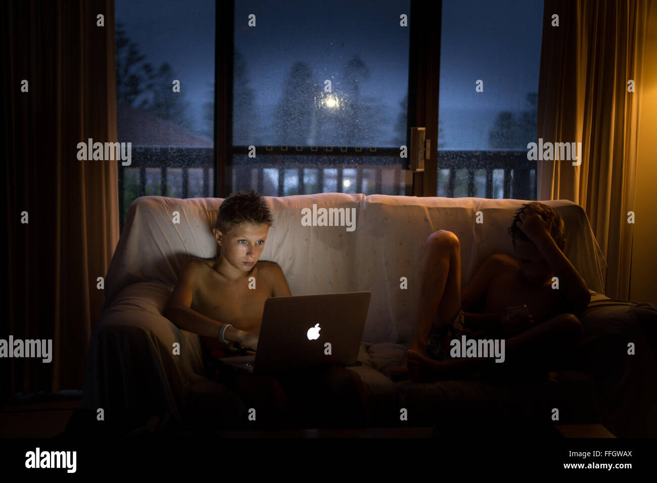A boy using a laptop on a rainy dark evening Stock Photo