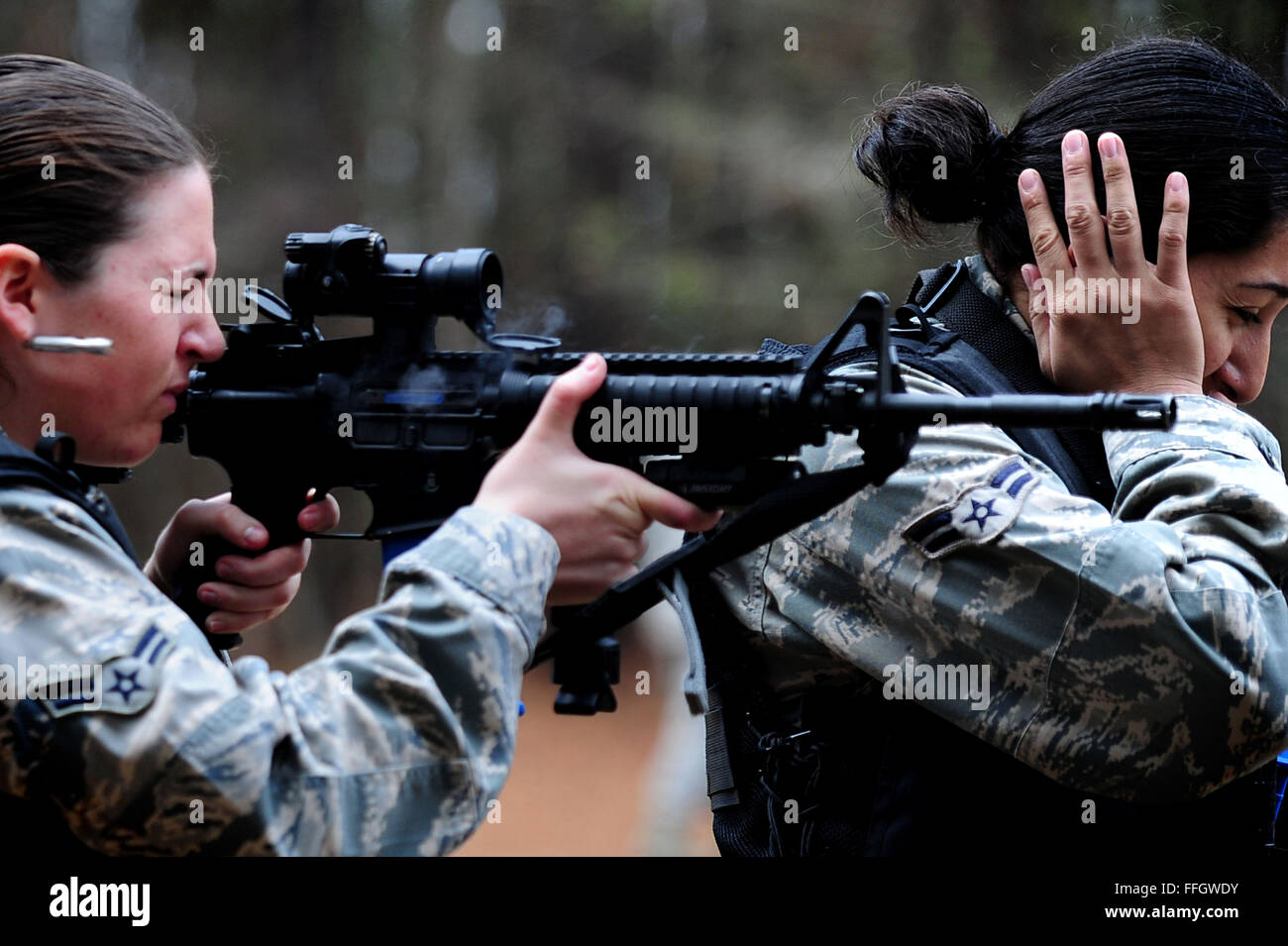 Airman 1st Class Yajaira Aguiar covers her ears while Airman 1st Class Samantha Rasch fires her M4A1 during 'Shoot, Move, Communicate' training course, Feb. 16, Joint Base Charleston - Air Base, S.C.  The training teaches airmen to react to a hostile shooter by using cover and effective communication to maneuver and engage the target. Aguiar and Rasch is from the 628th Security Forces Squadron. Stock Photo